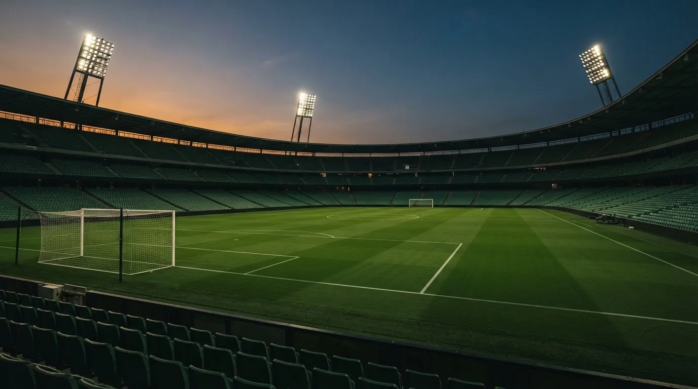An empty football stadium with floodlight masts at dusk